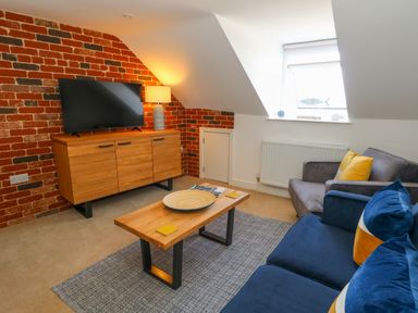 A living room with a blue sofa and wooden coffee table near a television on a wooden cabinet at The Loft @ No36 in Weymouth