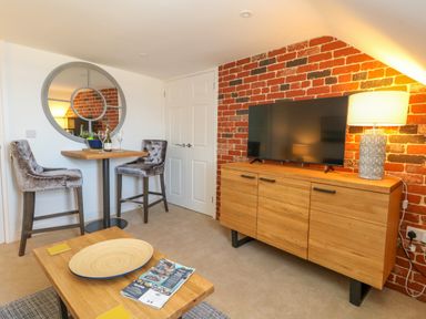 A small dining area with two bar stools and round mirror next to a wooden cabinet with a TV and lamp at The Loft @ No36 in Weymouth