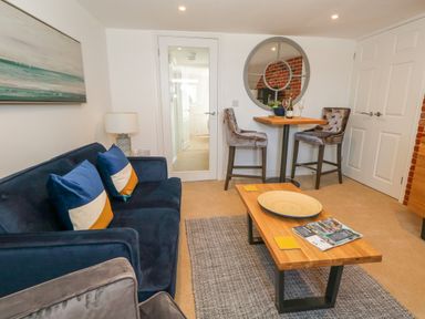 A living room with a blue sofa, a wooden coffee table, a small dining table with two chairs, a lamp, and a round wall mirror at The Loft @ No36 in Weymouth