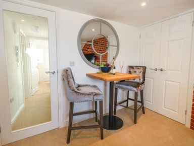 A small dining area with a wooden table, two upholstered high chairs, and a round wall mirror at The Loft @ No36 in Weymouth