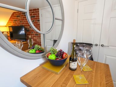 A dining table with a bowl of fruit two wine glasses and a bottle of wine in a room with a mirror and a brick wall at The Loft @ No36 in Weymouth
