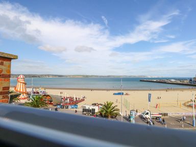 A beach with sandy shore and sea with people walking near a promenade and a colorful helter skelter at The Loft @ No36 in Weymouth