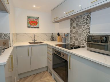 A modern kitchen with white countertops a stainless steel sink an oven stove a microwave and patterned tile backsplash at The Loft @ No36 in Weymouth