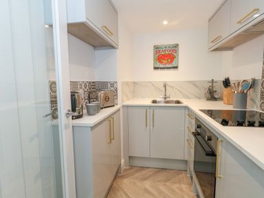 A kitchen with grey cabinets white countertops a stove toaster kettle sink and kitchen utensils at The Loft @ No36 in Weymouth
