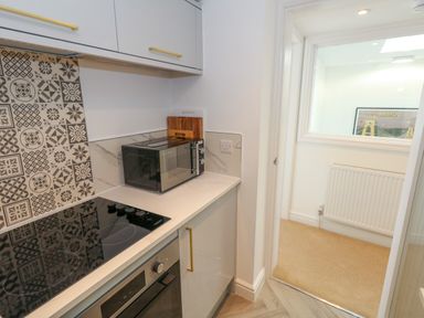 A kitchen countertop with a microwave oven and an electric stove next to a doorway showing a room with a radiator and a framed picture at The Loft @ No36 in Weymouth