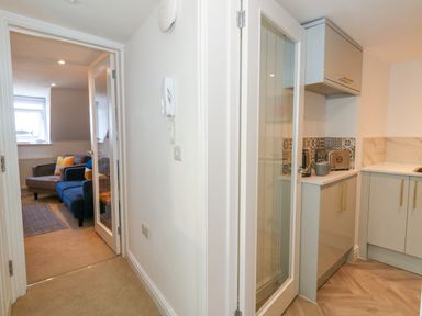 A hallway leading to a living room with sofas and a kitchen area with cabinets and appliances at The Loft @ No36 in Weymouth