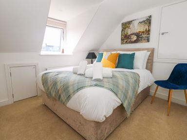 A bedroom with a bed covered with pillows and rolled towels a window a chair and a painting on the wall at The Loft @ No36 in Weymouth