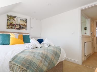 A bedroom with a bed with colorful pillows and a checked blanket with rolled towels on top and a painting on the wall at The Loft @ No36 in Weymouth