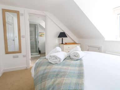 A bedroom with a bed laid with towels and a plaid blanket near a door to a bathroom with a glass shower at The Loft @ No36 in Weymouth