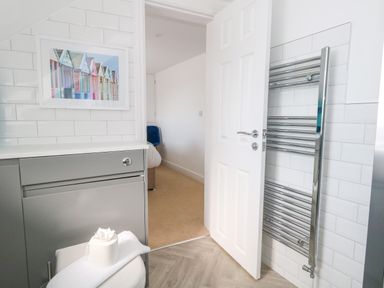 A bathroom with a gray cabinet a towel radiator and an open door showing a bedroom at The Loft @ No36 in Weymouth
