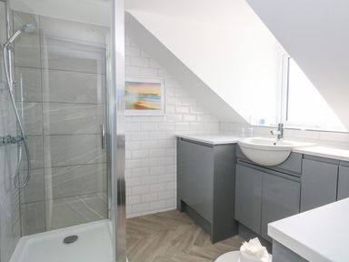 A bathroom with a shower enclosure and a sink with gray cabinets under a sloped ceiling at The Loft @ No36 in Weymouth