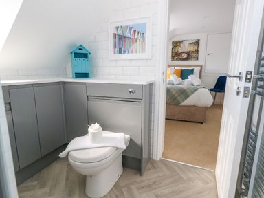 A bathroom with a toilet and grey cabinets next to a bedroom with a bed and a blue chair at The Loft @ No36 in Weymouth