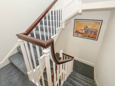 A carpeted staircase with white balusters and wooden handrails with a framed picture on the wall at The Loft @ No36 in Weymouth