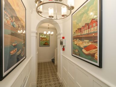 A narrow hallway with patterned floor tiles chandeliers and framed posters on the walls at The Loft @ No36 in Weymouth