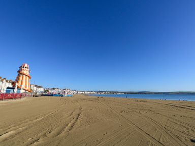 A sandy beach with a carnival slide and buildings along the shore at The Loft @ No36 in Weymouth
