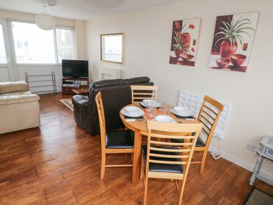 A living room with wooden dining table set and sofas facing a television at Freshwater East in Freshwater East