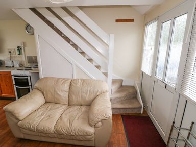 A small living area with a beige leather sofa next to a staircase and a door with windows and blinds at Freshwater East in Freshwater East