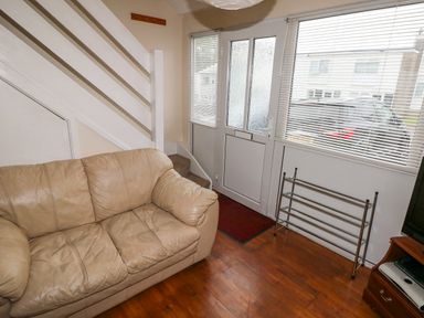 A living room with a beige sofa wooden floor a white staircase and a front door with blinds at Freshwater East in Freshwater East