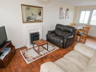 A living room with leather sofas a small wooden table a fireplace a wall mirror TV and a dining table with chairs at Freshwater East in Freshwater East
