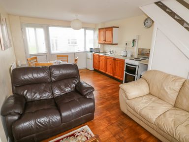 A living room with brown and beige sofas and an open kitchen with wooden cabinets and a dining table at Freshwater East in Freshwater East