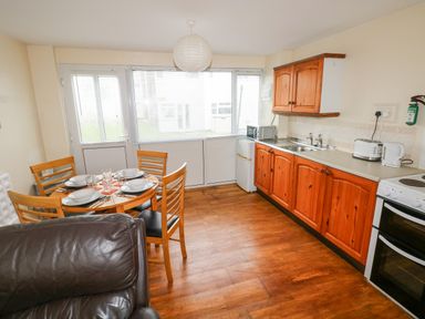 A kitchen and dining area with wooden cabinets a dining table set for four and kitchen appliances at Freshwater East in Freshwater East