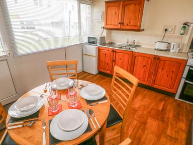 A kitchen with wooden cabinets a round dining table set for four and appliances at Freshwater East in Freshwater East