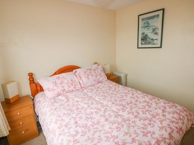 A bedroom with a bed covered in pink floral bedding two wooden bedside tables with lamps a framed picture on the wall at Freshwater East in Freshwater East
