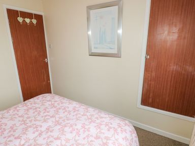 A bedroom with a bed covered in a pink patterned duvet two wooden doors and a framed picture on the wall at Freshwater East in Freshwater East