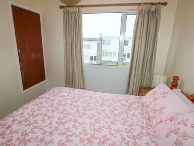 A bedroom with a bed covered in pink floral bedding and a window with curtains at Freshwater East in Freshwater East