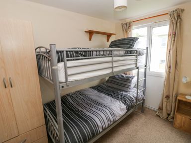 A bedroom with a metal bunk bed a wooden wardrobe a small wooden bedside table and a window with curtains at Freshwater East in Freshwater East