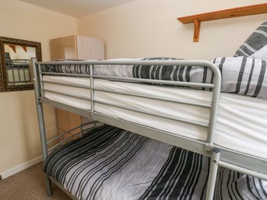 A bedroom with a metal bunk bed with striped bedding a wooden shelf a wardrobe and a framed mirror on the wall at Freshwater East in Freshwater East