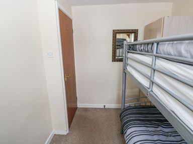 A small bedroom with a bunk bed a wooden door and a mirror on the wall at Freshwater East in Freshwater East