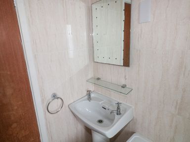 A bathroom with a pedestal sink two taps a glass shelf a mirror a towel ring and tiled walls at Freshwater East in Freshwater East