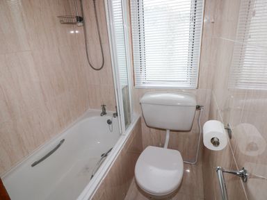 A bathroom with a bathtub a toilet a window with blinds and tiled walls at Freshwater East in Freshwater East