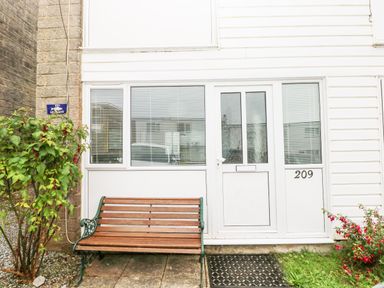A front entrance with white door and windows a wooden bench and plants outside at Freshwater East in Freshwater East