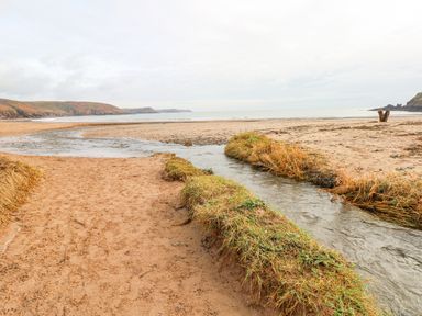 A sandy beach with a small stream flowing into the sea and grassy banks at Freshwater East in Freshwater East