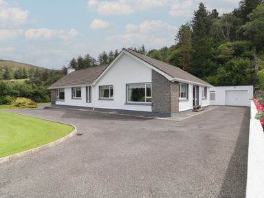 A single-story house with a driveway and garage surrounded by trees at Nelly's House in Gortahork County Donegal