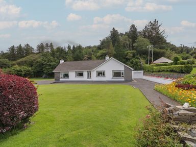 A single story house with a driveway and a garage surrounded by grass and trees at Nelly's House in Gortahork County Donegal