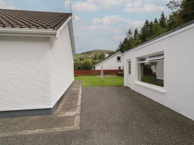 An outdoor space between white buildings with a paved area and grassy lawn at Nellys House in Gortahork County Donegal