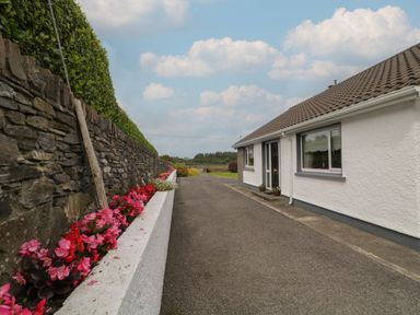 A driveway beside a white house with flower beds and a stone wall at Nelly's House in Gortahork County Donegal