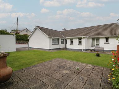 A backyard with a tiled patio lawn a bench and flowering plants at Nelly's House in Gortahork County Donegal
