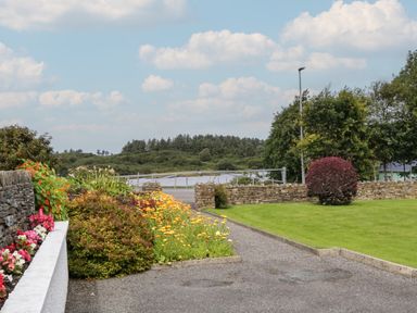 A garden with flower beds shrubs green grass and a stone wall with a gate and trees at Nelly's House in Gortahork County Donegal