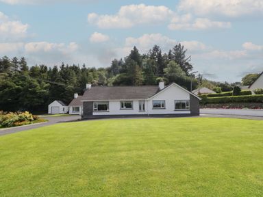 A detached house with a large green lawn and trees in the background at Nelly's House in Gortahork County Donegal
