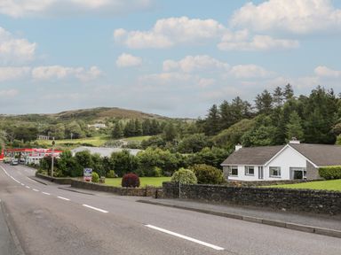 A road with a house lawn and trees beside it and a gas station in the distance at Nelly's House in Gortahork County Donegal