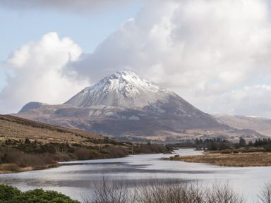 A snow capped mountain with a river in the foreground and cloudy sky at Nelly's House in Gortahork County Donegal