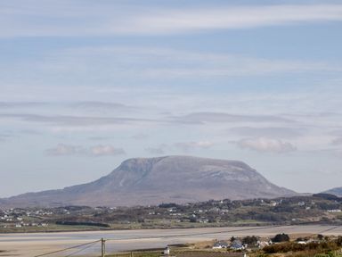 A landscape view of a mountain with scattered houses and a body of water in the foreground at Nelly's House in Gortahork County Donegal