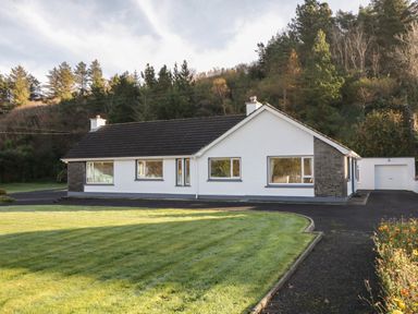 A single-story house with white walls and a dark roof next to a driveway and lawn at Nelly's House in Gortahork County Donegal