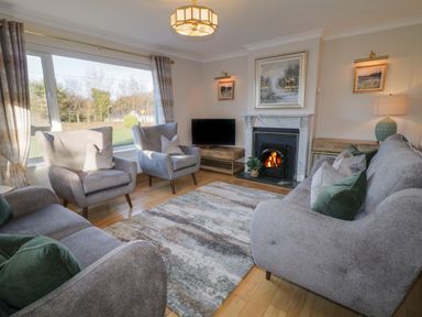A living room with gray sofas and armchairs a fireplace and a television at Nelly's House in Gortahork County Donegal