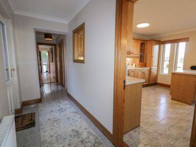 A hallway with a rug and a view into a kitchen with wooden cabinets at Nelly's House in Gortahork County Donegal