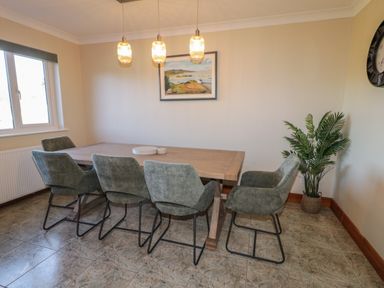 A dining room with a wooden table surrounded by six grey chairs a potted plant on the floor and a painting on the wall at Nelly's House in Gortahork County Donegal